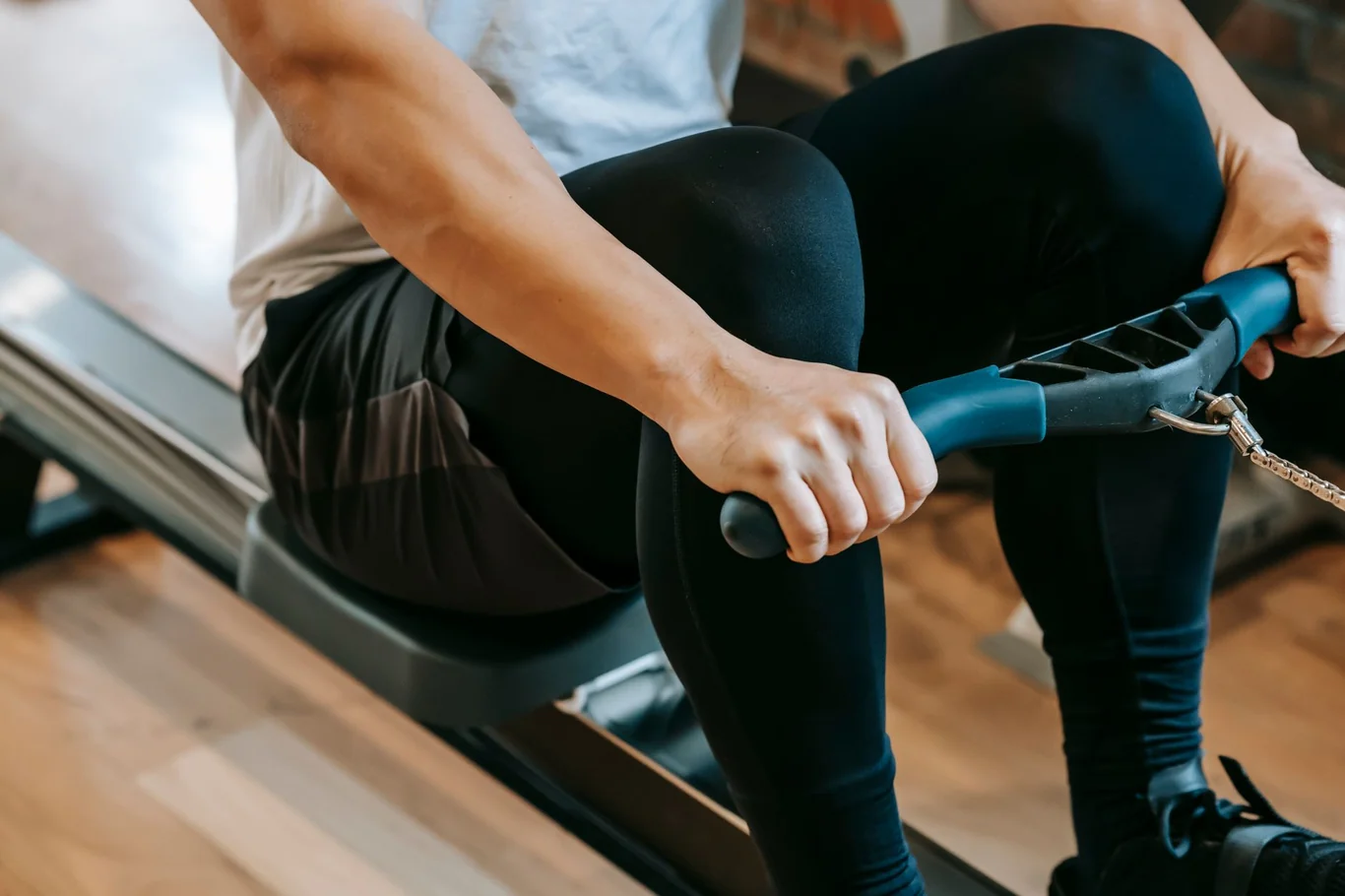 Rower's hands gripping the handle while seated on the padded seat of a sliding rail machine