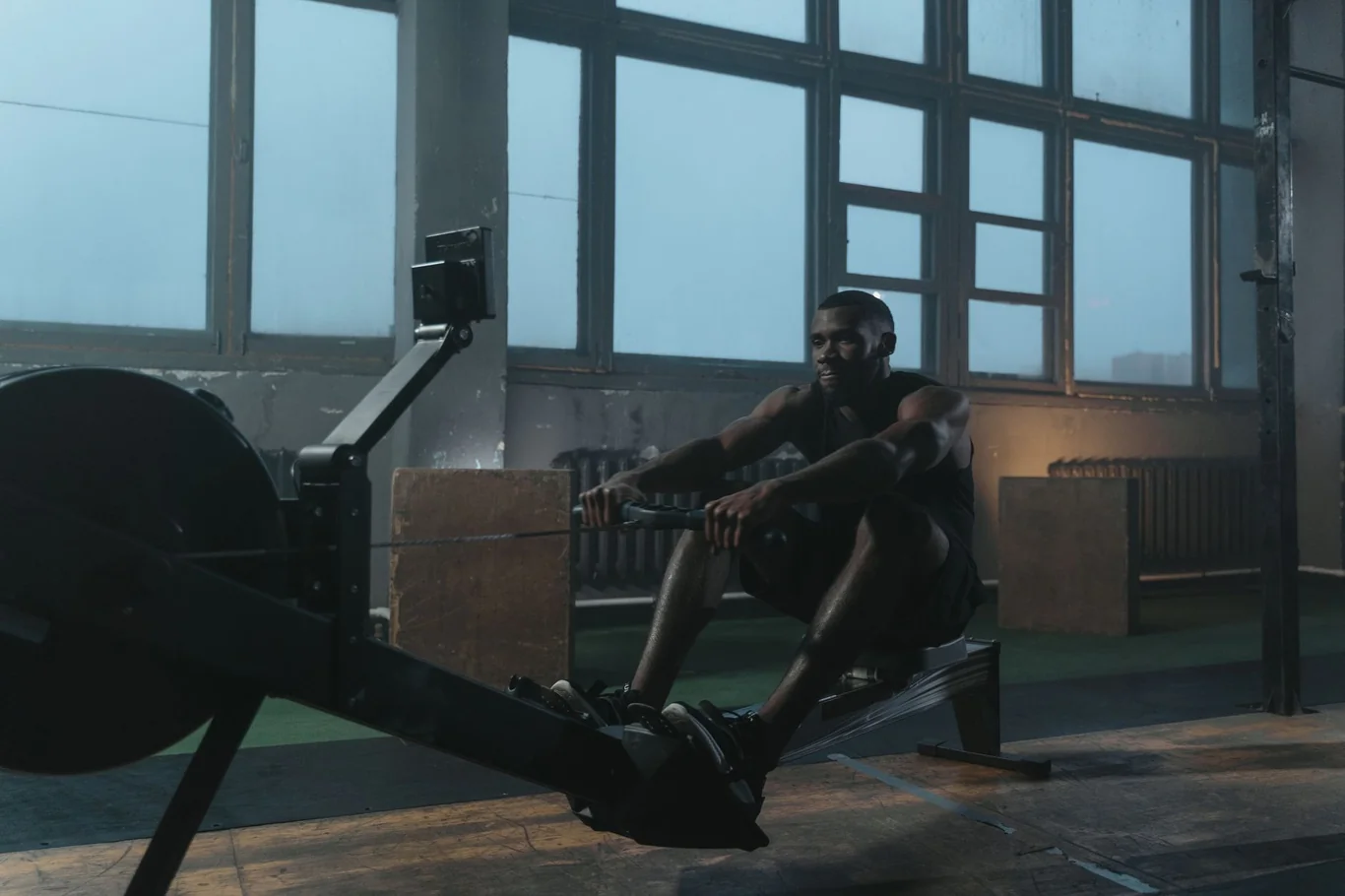 Man rowing on an indoor rowing machine in a dimly lit warehouse gym