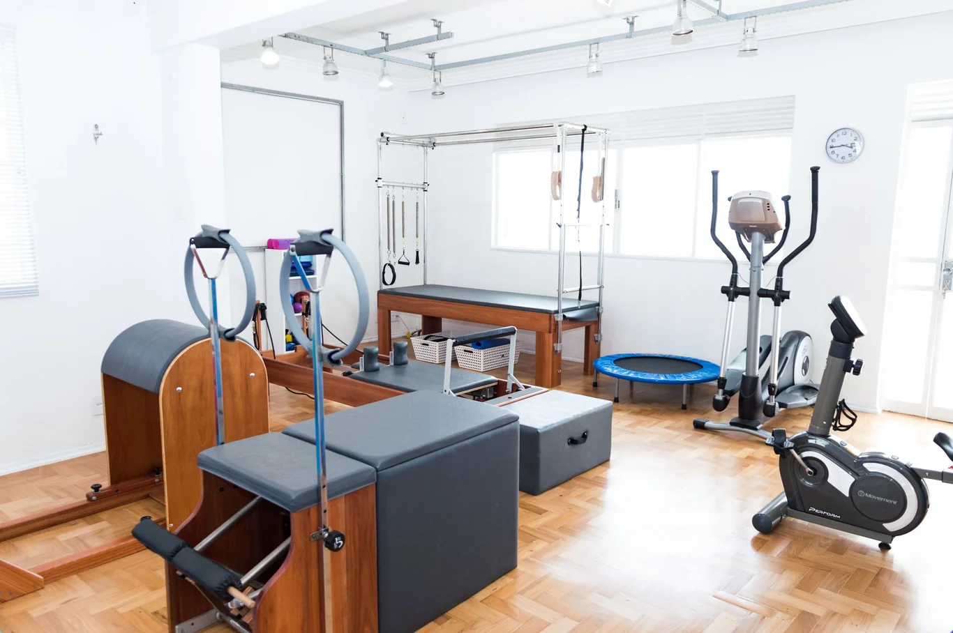 Home gym room with a reformer, elliptical, mini trampoline, and exercise bike on wood flooring