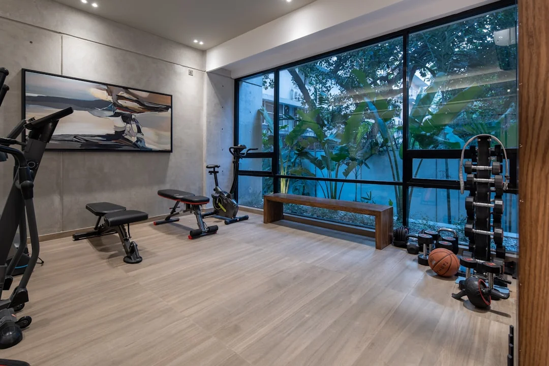 Modern home gym with floor to ceiling windows, an exercise bike, and a wooden bench with dumbbells