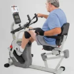 Man seated on the Innova RCT2025 recumbent cross trainer, rear angle showing the adjustable swivel seat and backrest