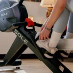 Close-up of a woman clipping into the Sole rower foot pedal and handle, SOLE branding on frame
