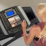 Close-up of a hand adjusting the NordicTrack T 6.5 S console with a tablet propped on the device shelf during a workout