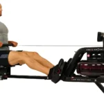 Woman rowing the Sunny Obsidian Surge water rower with water tank visible