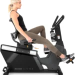 Woman using the 3G Cardio Elite RB X recumbent bike in side profile, showing seated riding position and low step-through frame