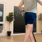 Rear view of a man walking on the Sunny Treadpad Slim with trekking poles in a living room