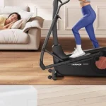 Woman using the Merach elliptical quietly while a partner sleeps on the couch nearby