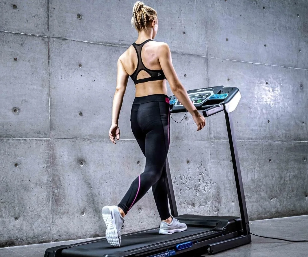 XTERRA Fitness TRX1000 folding treadmill in use in a concrete-walled home gym, showing the XTRA Soft cushioned deck and folding frame