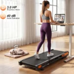 Woman using the Vitalwalk Apollo 11-Vibe walking pad at a standing desk with a cat resting nearby