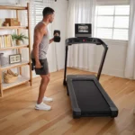 Person doing standing dumbbell curls beside a folded-down NordicTrack T Series 10 treadmill in a living room