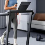 Woman using TOPUTURE treadmill with tablet propped on console shelf, front three-quarter view
