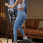 Woman using the ANCHEER elliptical from a rear angle in a dim living room