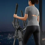 Woman using the OWLSKY elliptical in an evening city-view living room