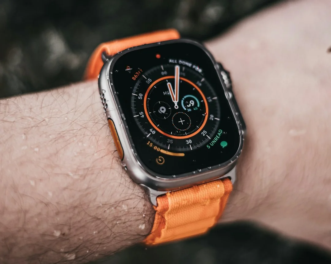 Apple Watch Ultra on a wrist with orange Alpine Loop band showing chronograph face