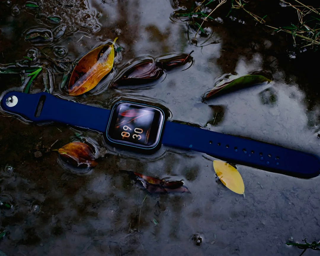Blue smartwatch lying in a shallow puddle of water with autumn leaves nearby