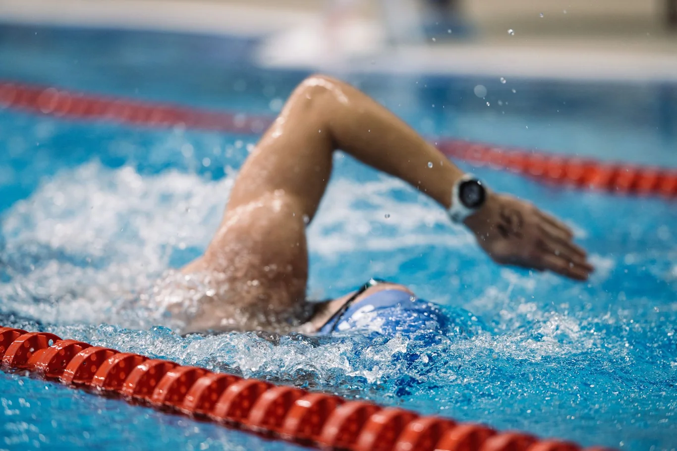 Swimmer doing freestyle in a pool with a sports watch visible on their wrist