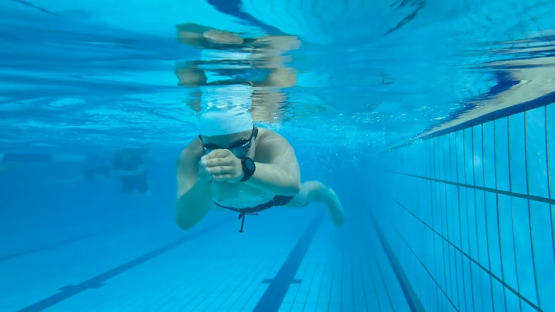 Swimmer underwater in a pool lane wearing a smartwatch and swim cap