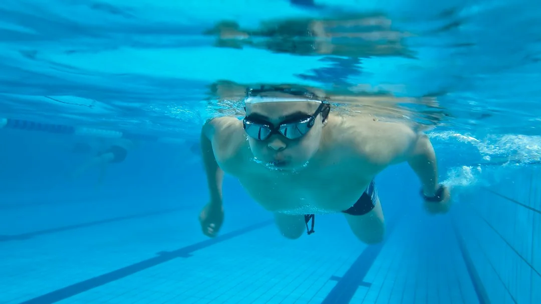 Man swimming laps underwater in an indoor pool wearing goggles