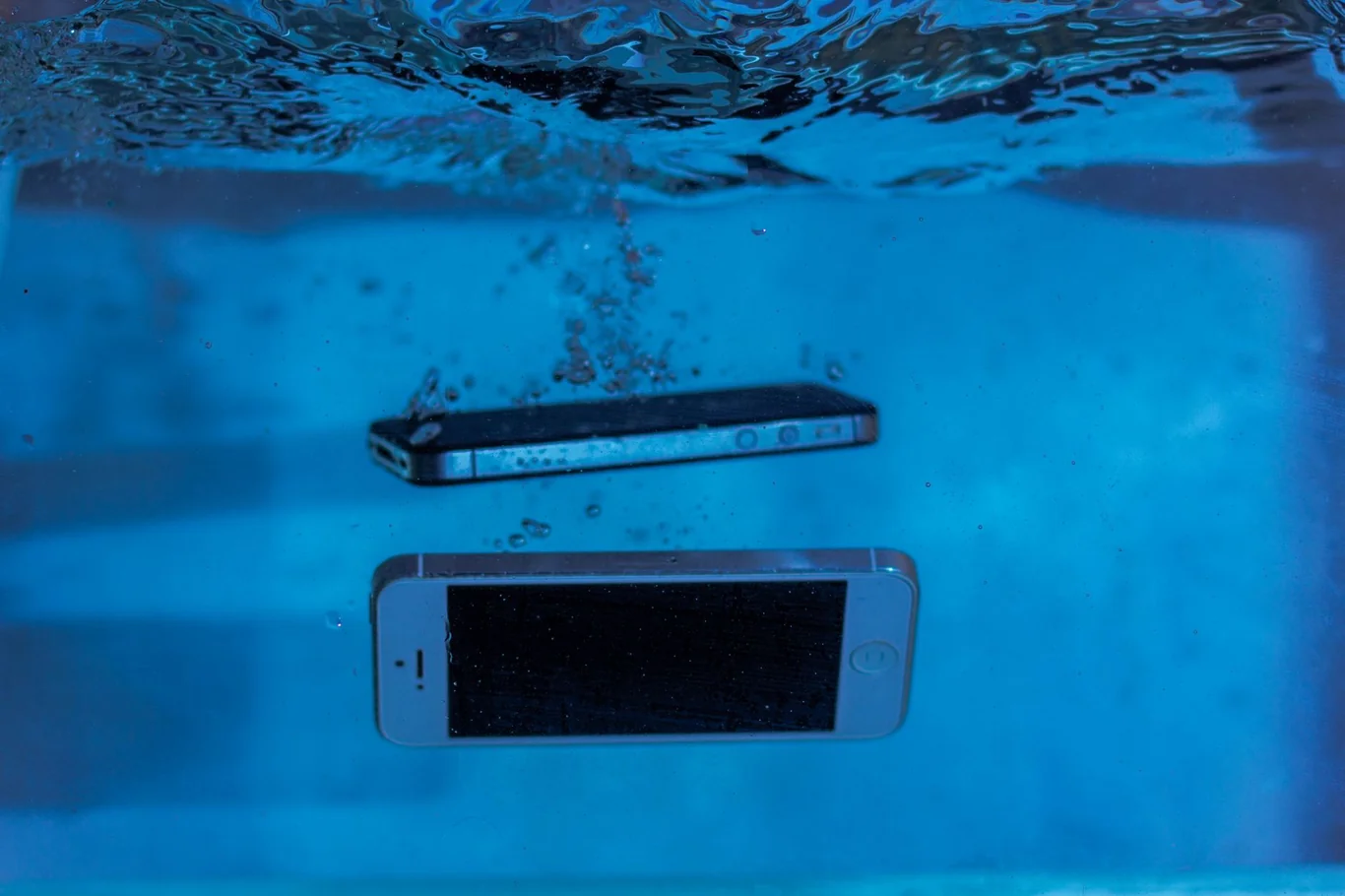 Two smartphones submerged underwater in a blue pool demonstrating water resistance testing