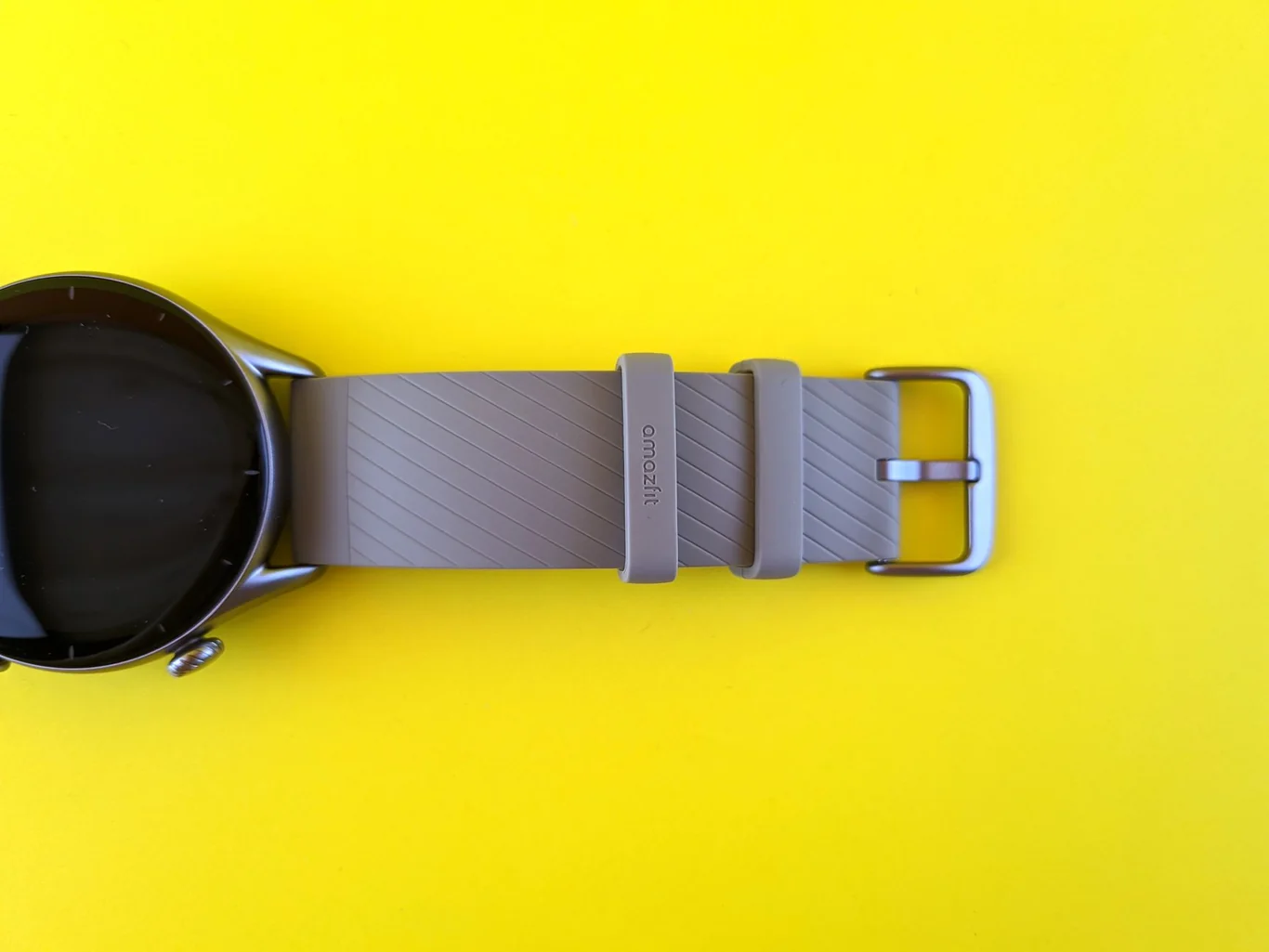 Smartwatch with a gray rubber band and metal buckle laid flat on a bright yellow background