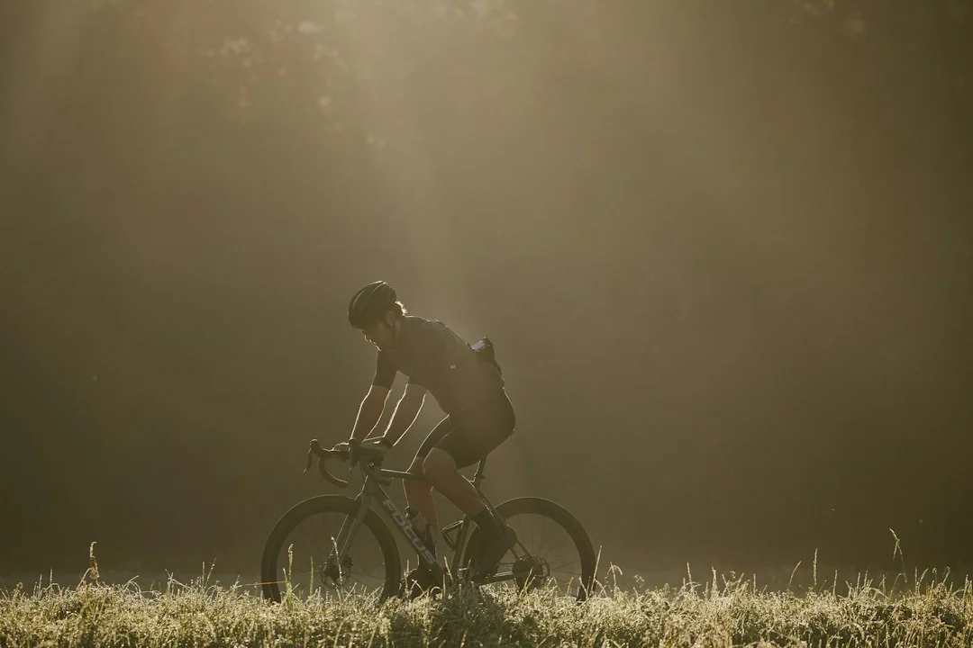Cyclist riding a road bike through a misty field in early morning light