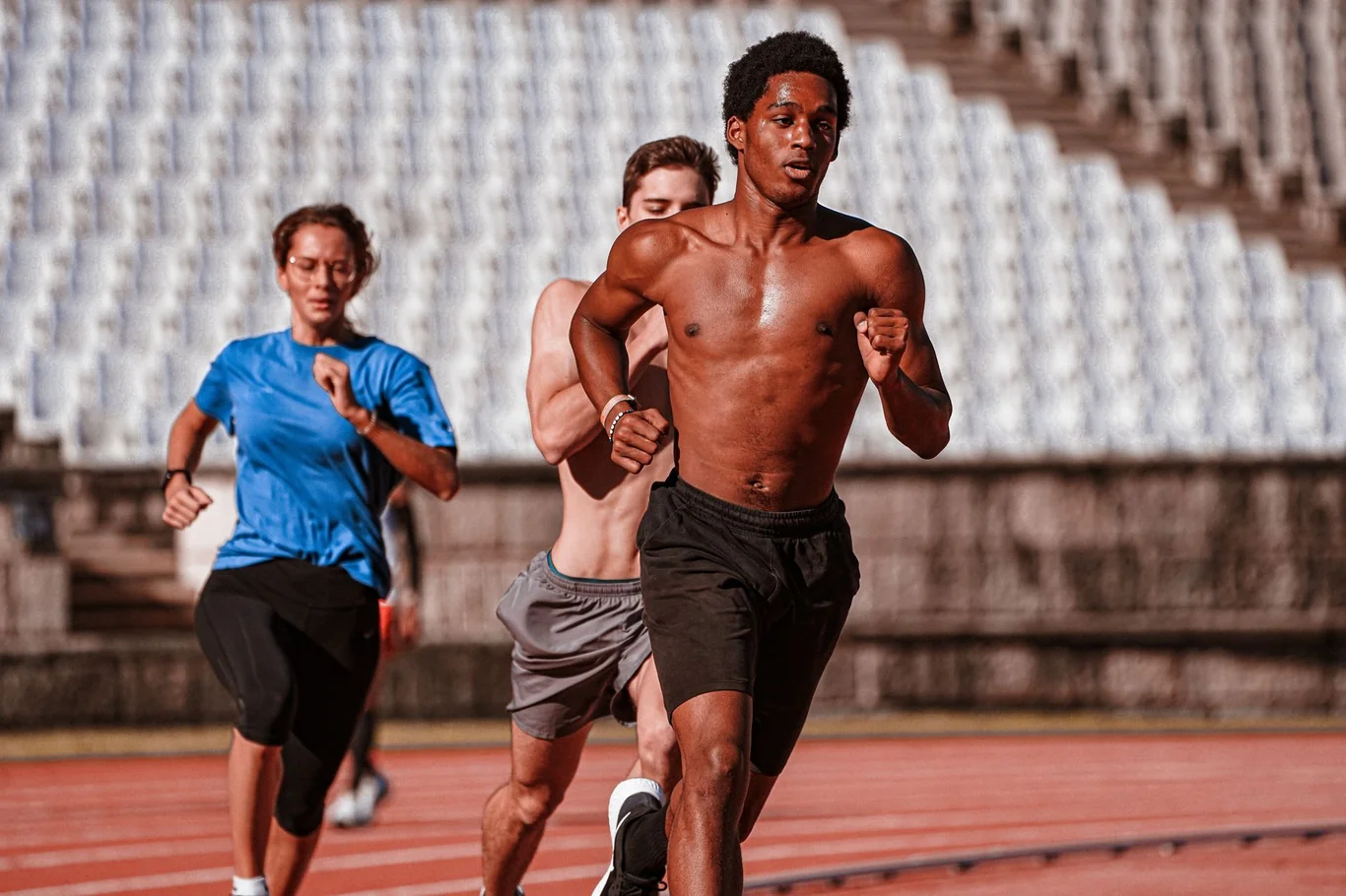 Three athletes running at high intensity on an outdoor track during a cardio training session