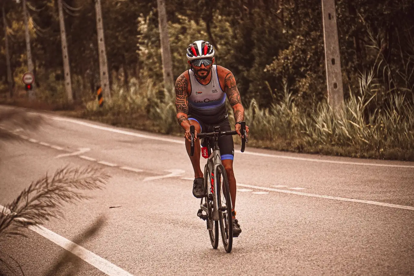 Tattooed triathlete racing on a road bike outdoors in a trisuit and helmet