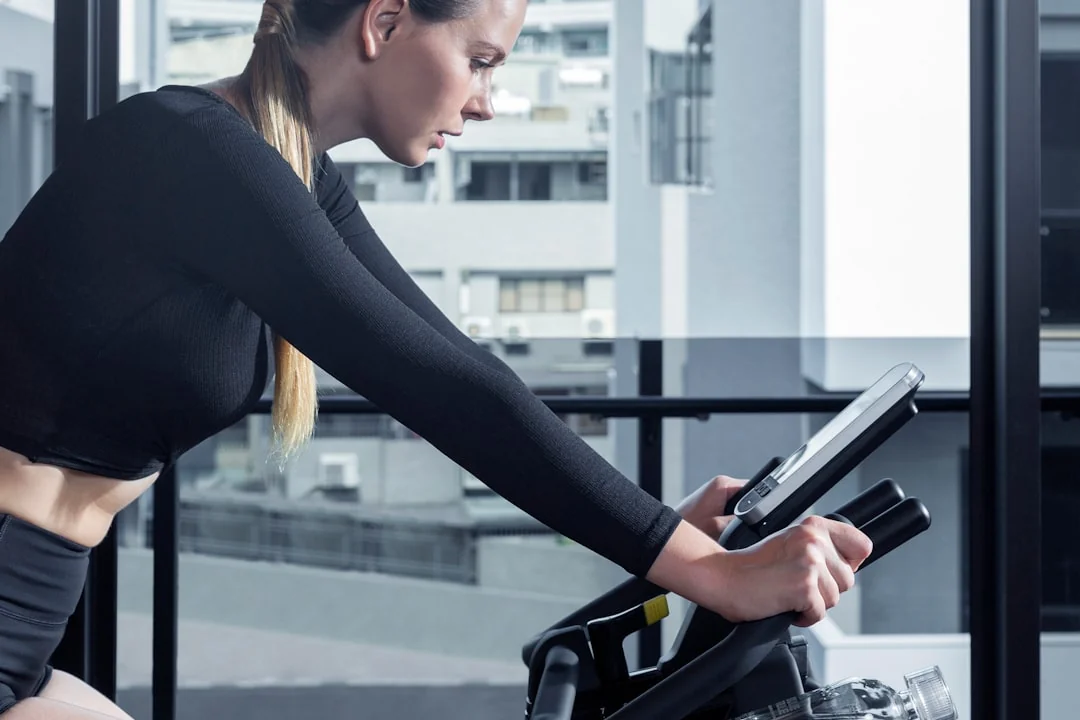 Woman in black athletic wear leaning forward on a stationary bike in a modern gym