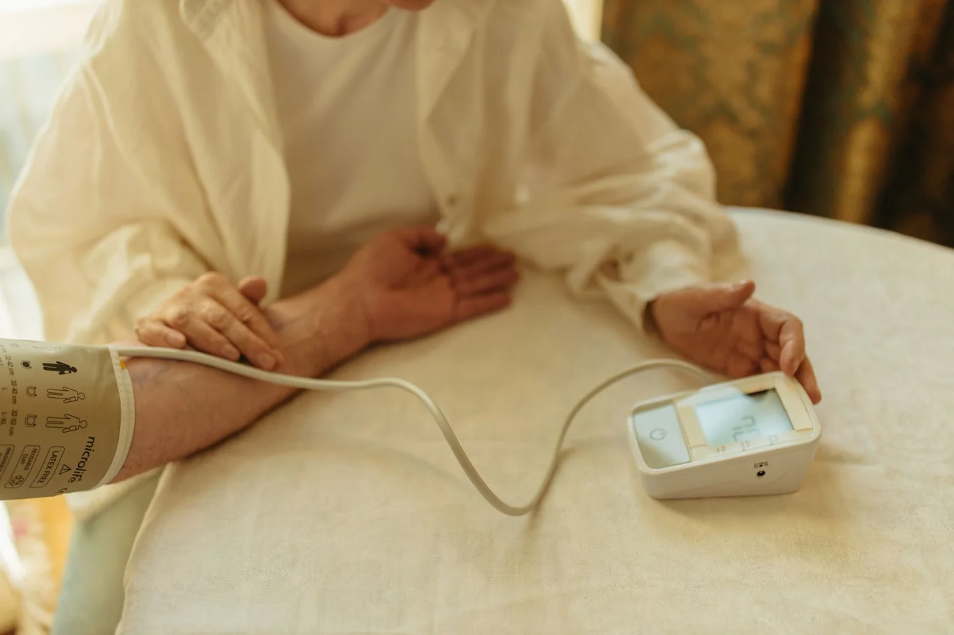 Person wearing an upper arm blood pressure monitor cuff while sitting at a table