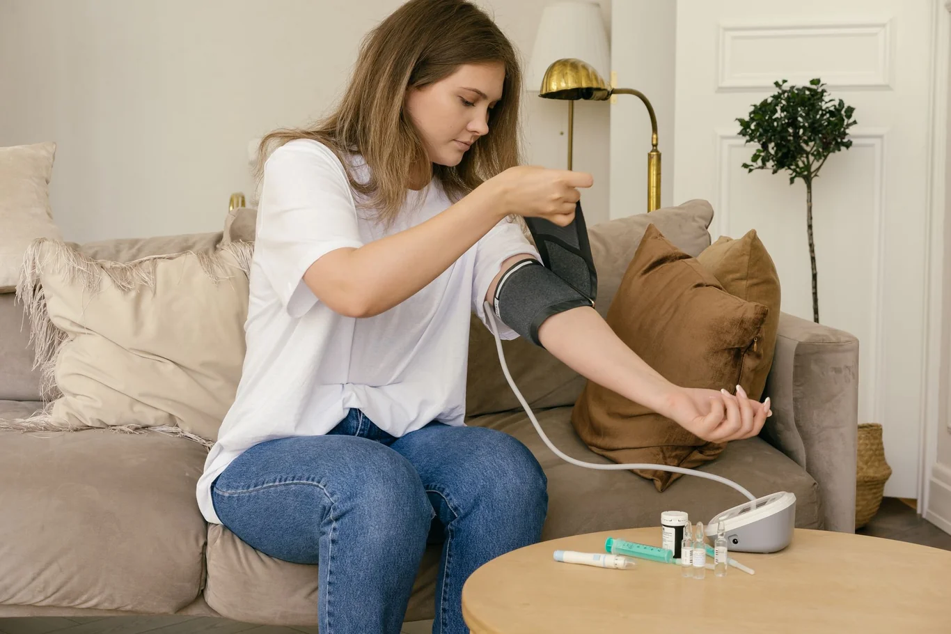 Young woman sitting on a couch applying an upper arm blood pressure cuff at home