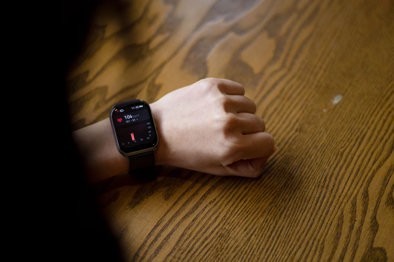 Apple Watch on a wrist displaying a heart rate reading of 104 on a wooden surface