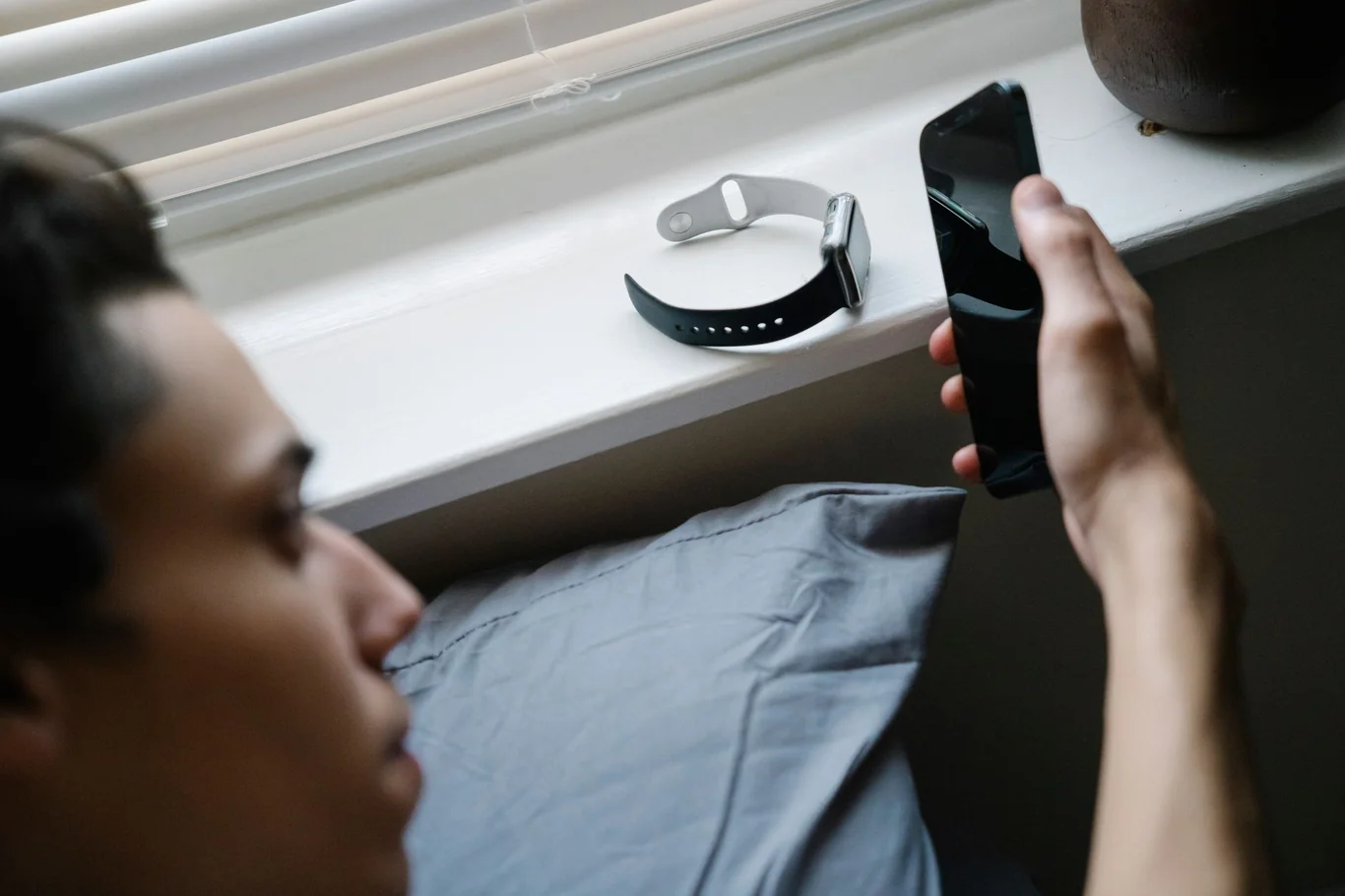 Person looking at a smartphone with an Apple Watch resting on a windowsill nearby