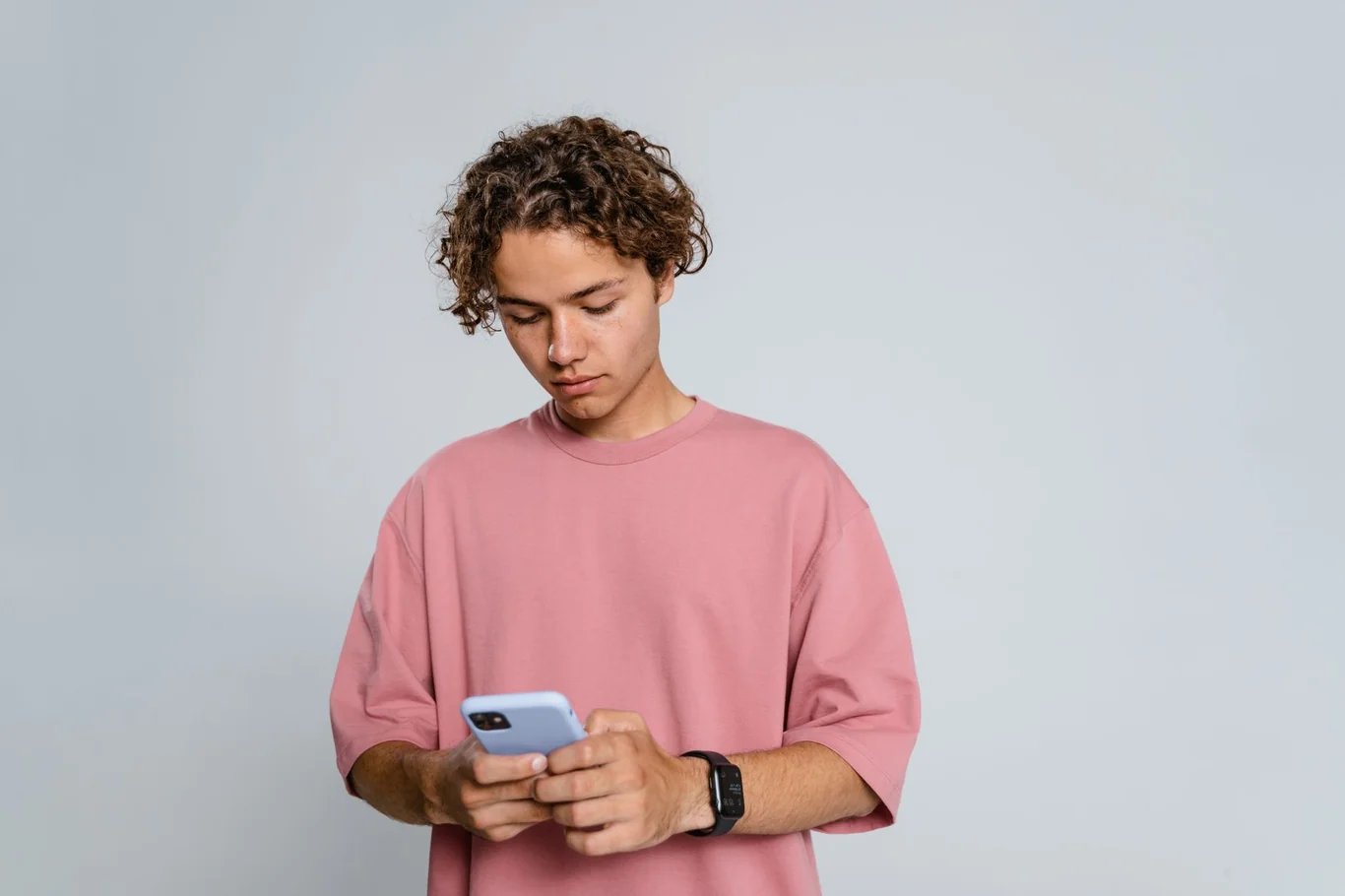 Young man in a pink shirt using a smartphone while wearing a black smartwatch on his wrist