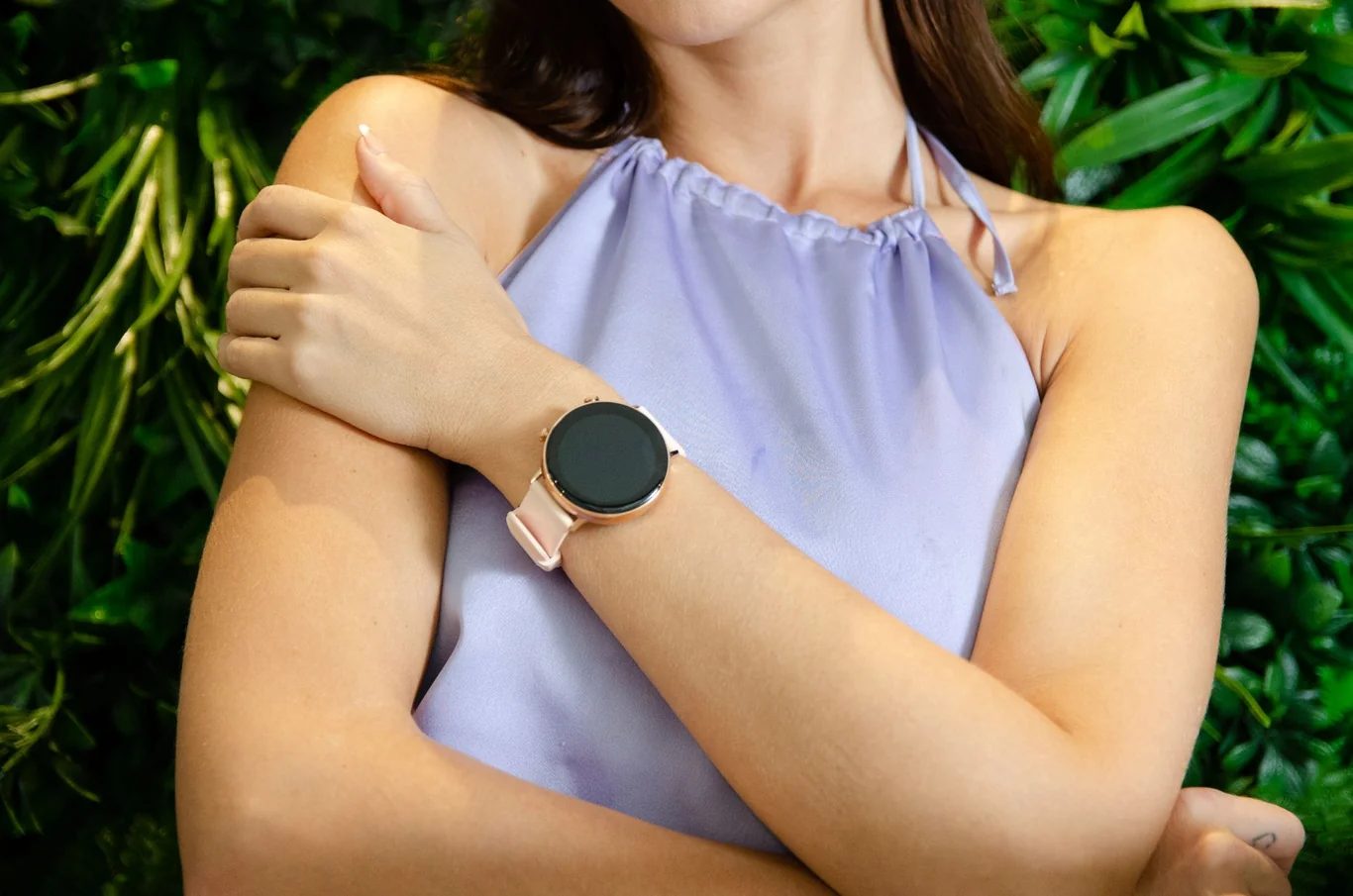 Woman wearing a rose gold round smartwatch with green foliage in the background