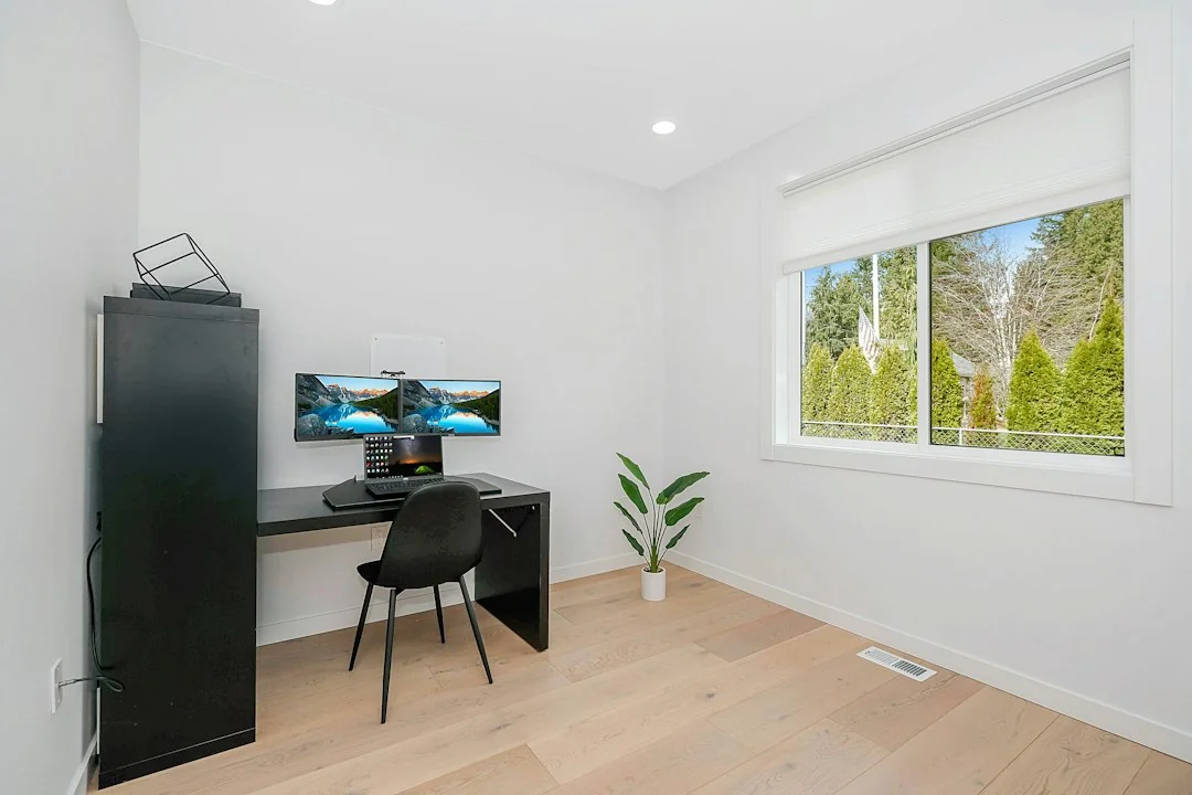 Clean home office desk setup with monitor, chair, and wood floor in a bright room