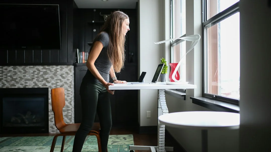 Woman standing at a white desk near a sunlit window in a modern home office