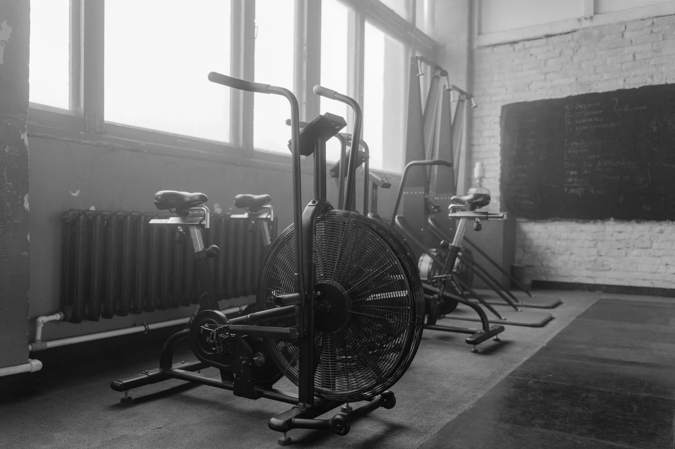 Row of air bikes in an empty gym with large windows and brick walls