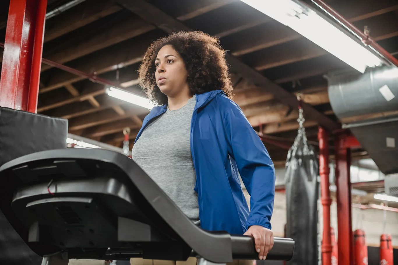 Woman in a blue jacket walking on a treadmill inside a gym