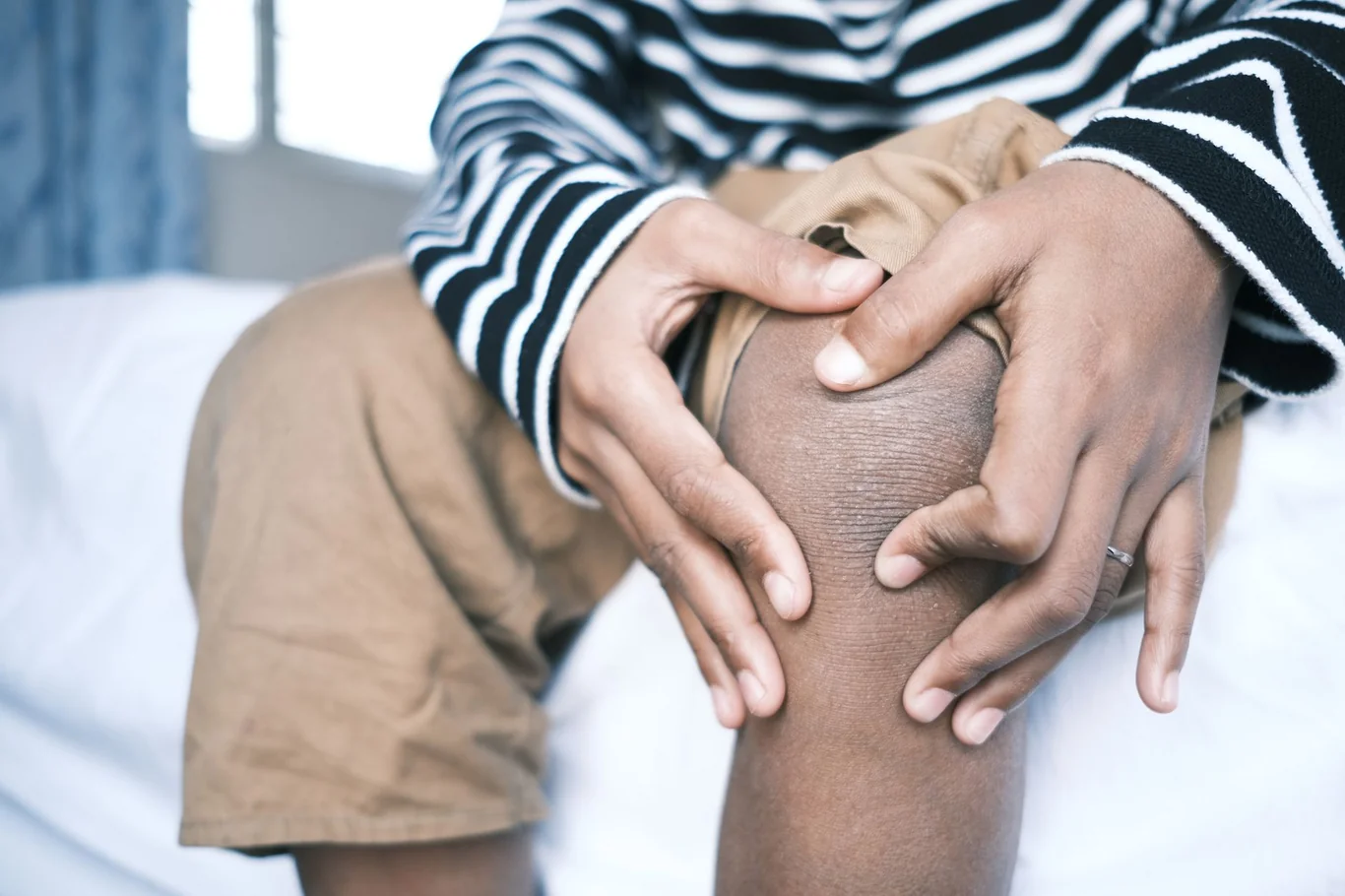 Person gripping a swollen bare knee with both hands while seated