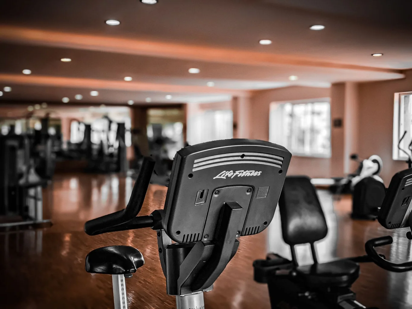 A stationary exercise bike in a well-lit commercial gym with cardio equipment in the background