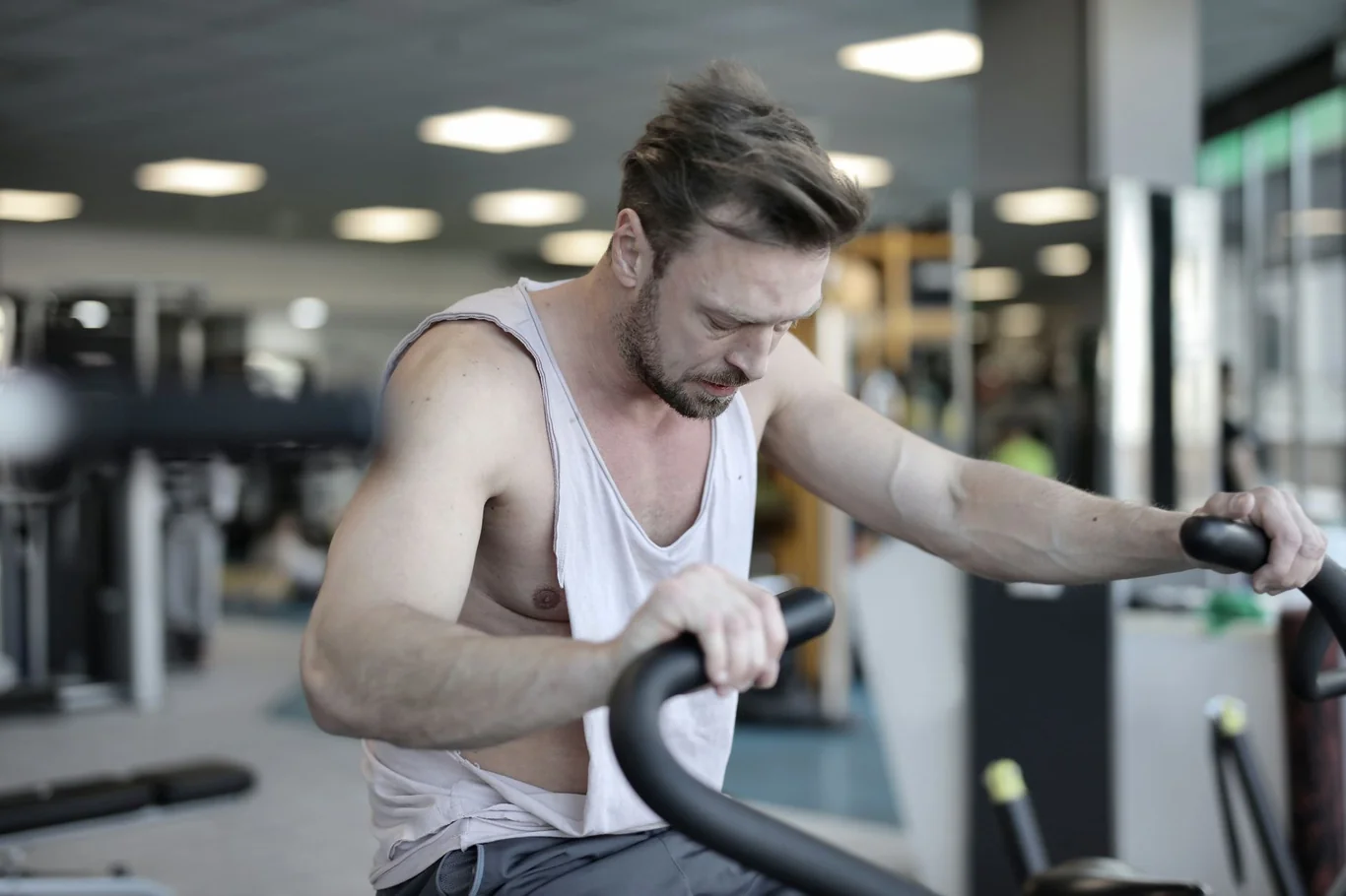 Man leaning over stationary bike handlebars during an intense gym workout