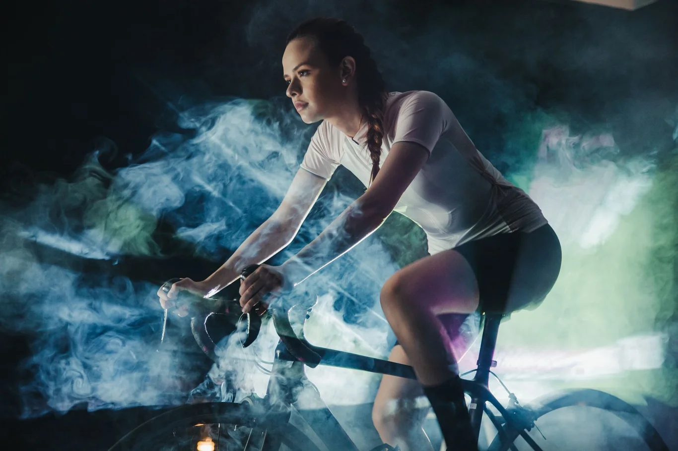 Woman leaning forward on an indoor exercise bike in a dark studio