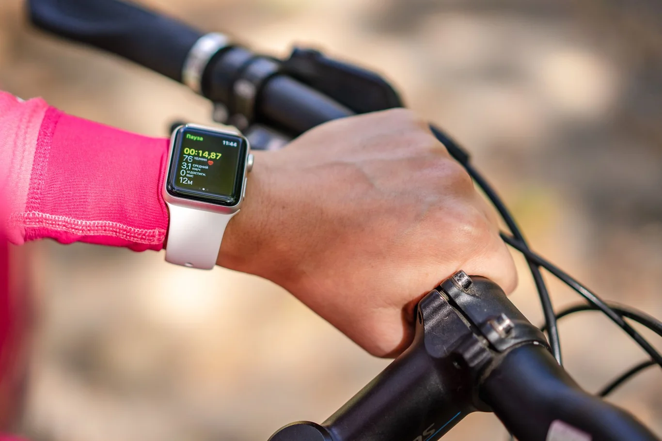 Cyclist checking workout stats on a smartwatch while gripping bike handlebars outdoors