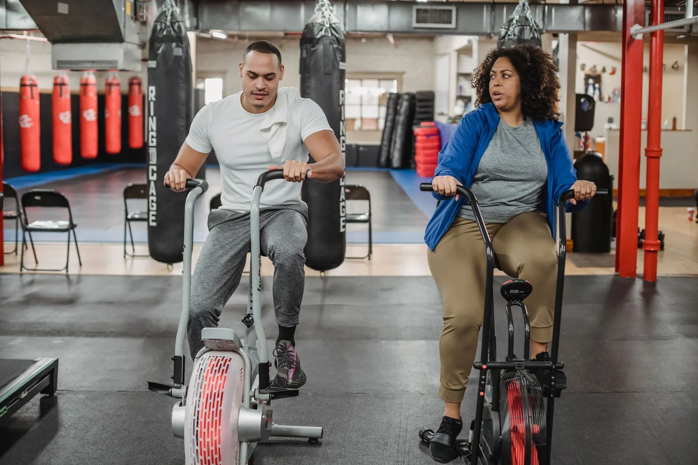 Man and woman riding exercise bikes in a gym, man wearing a fitness tracker on his wrist