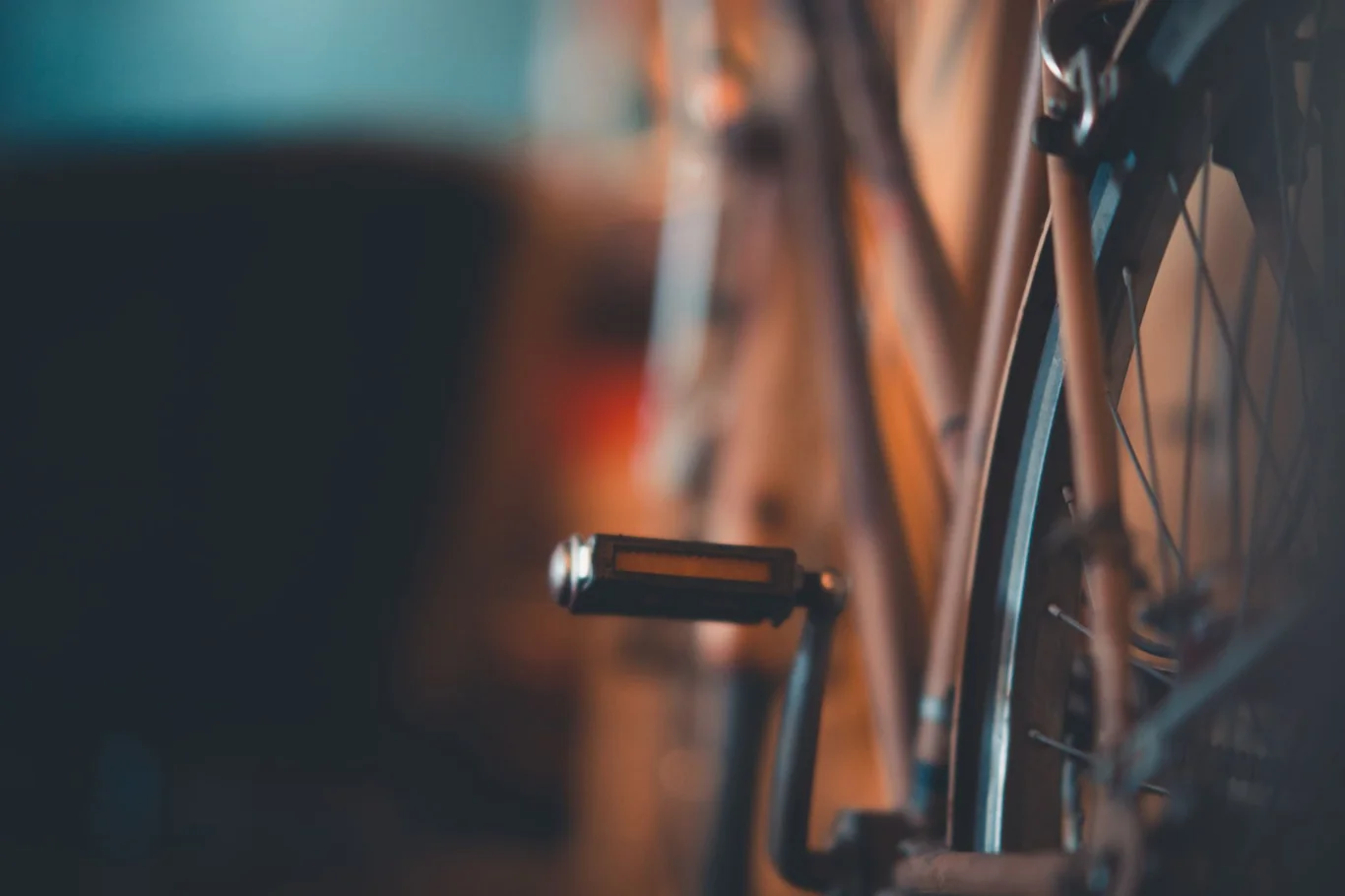 Close-up of a bicycle pedal and wheel spokes in a dimly lit indoor setting