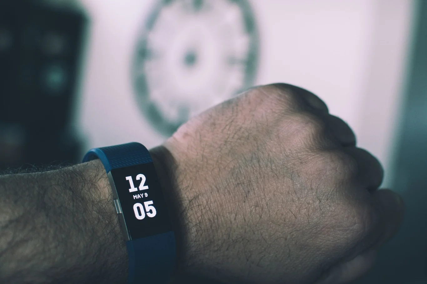 Blue fitness tracker on a wrist displaying time on a dark screen