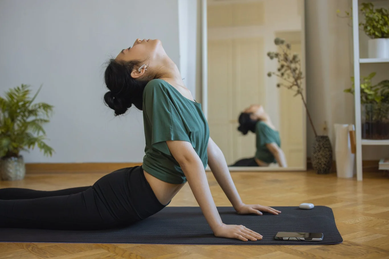 Woman doing a backbend yoga pose on a mat in front of a wall mirror in a home room