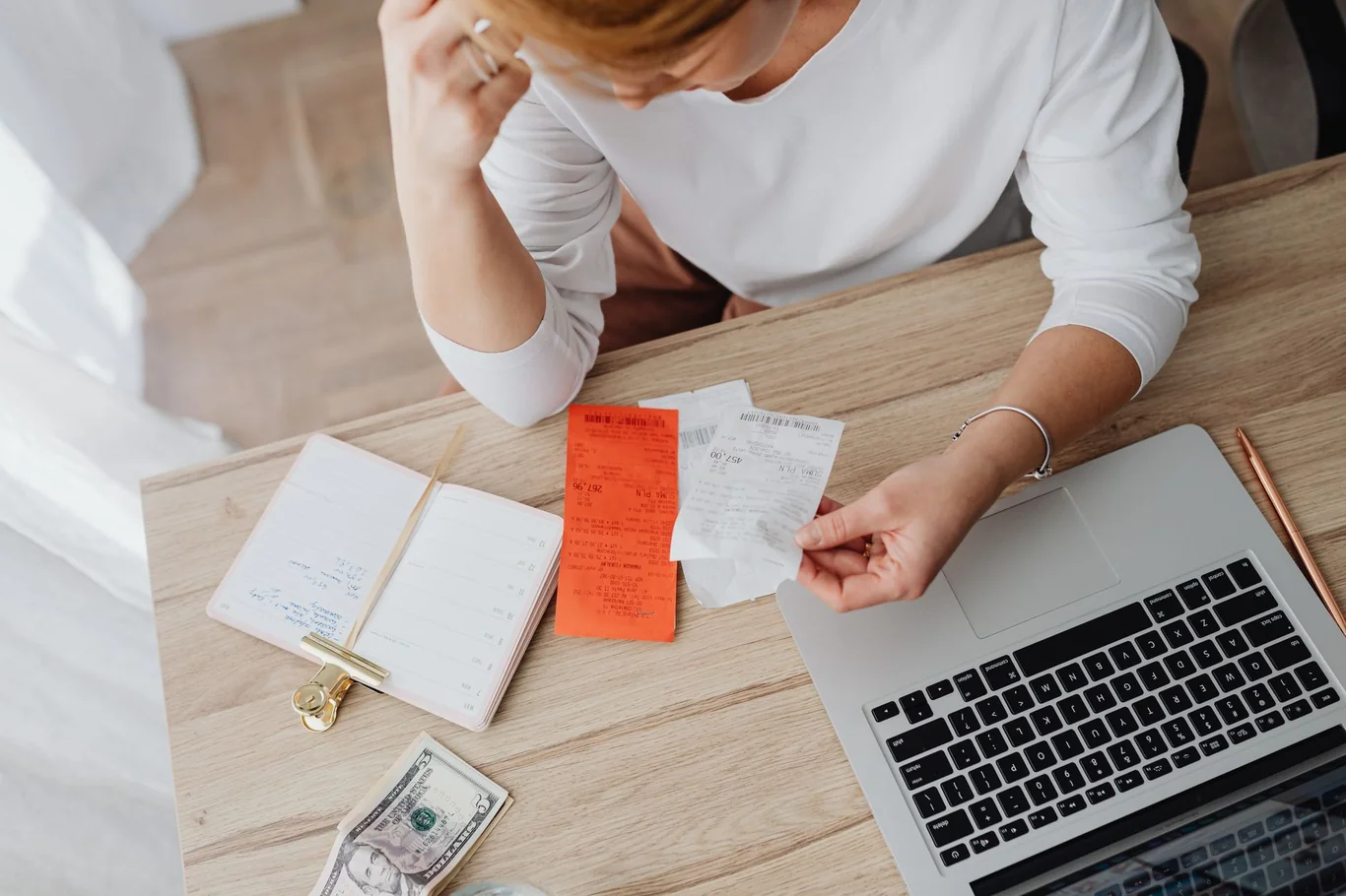 Person comparing paper receipts and cash next to an open laptop on a desk