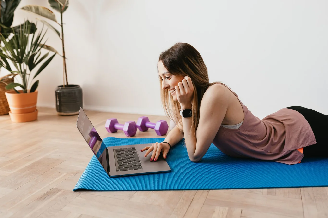 Woman on a yoga mat following a workout video on her laptop screen