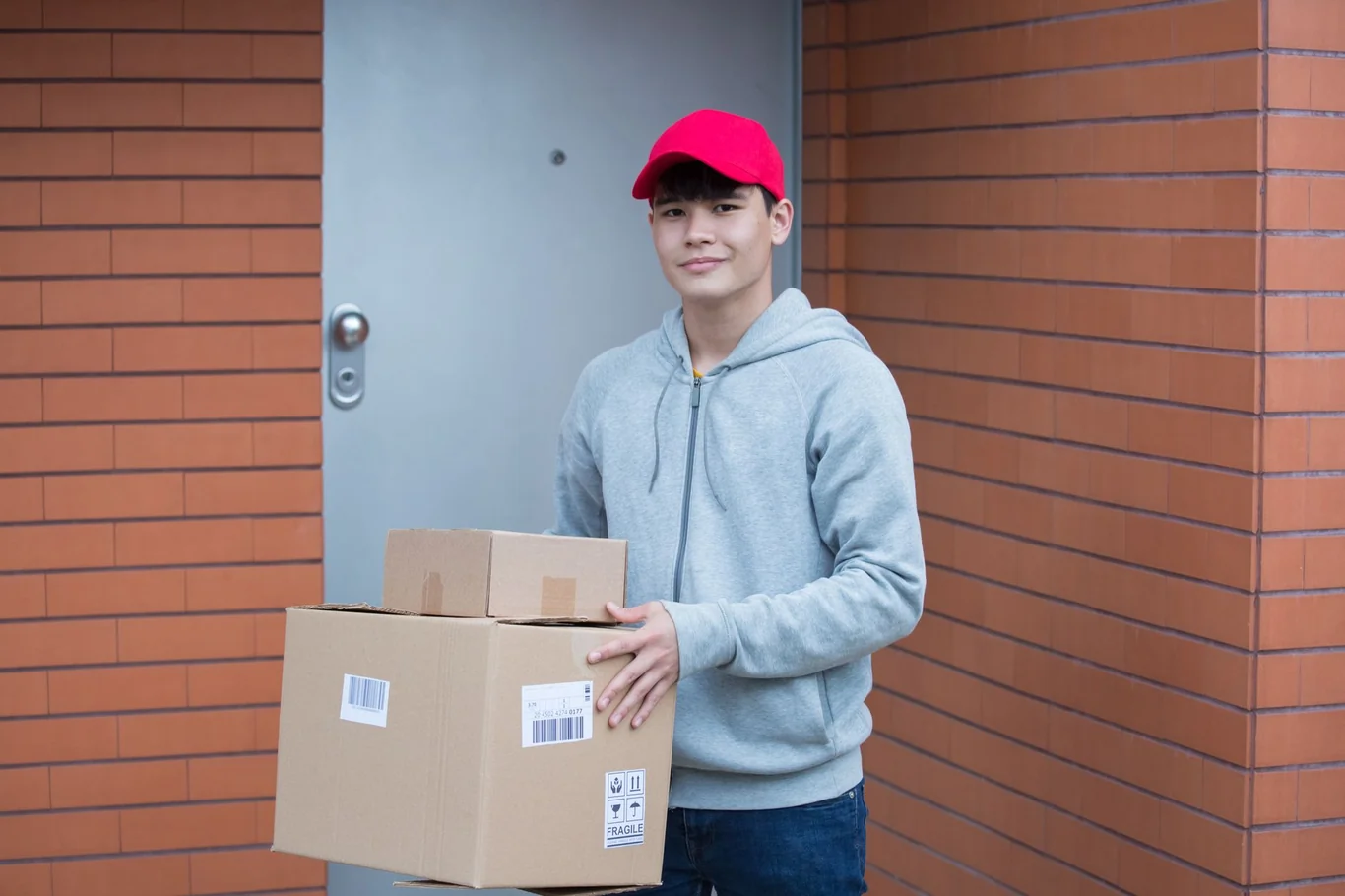 Delivery driver in a red cap carrying a large cardboard box to a front door